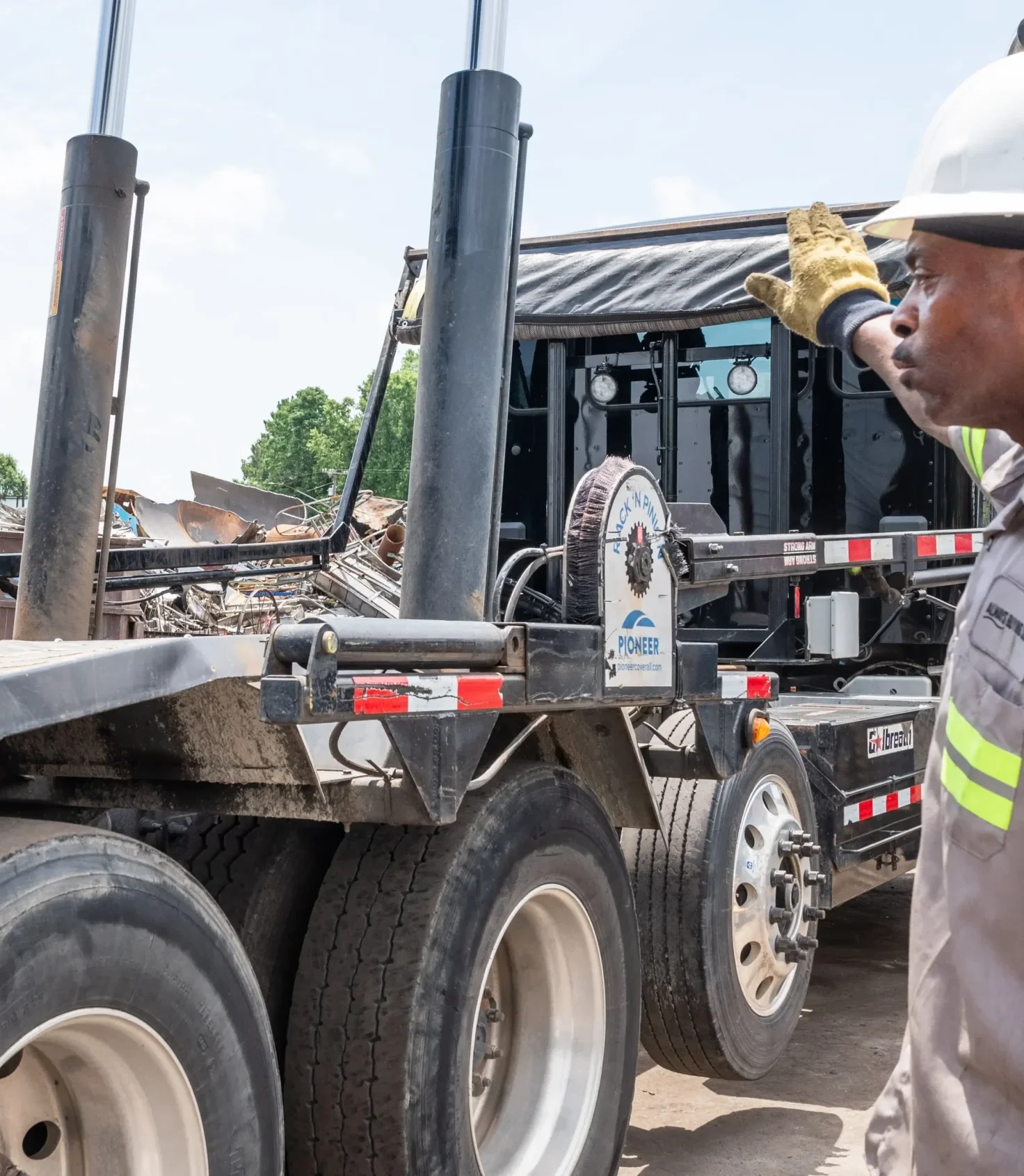 Worker wearing safety gear guiding a truck during loading operations at a scrap yard in Durham, NC.